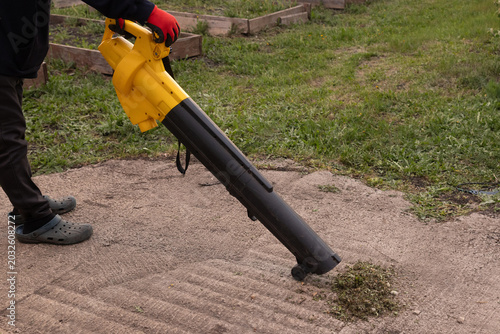Photos Worker uses electric blower to clear debris from garden path
