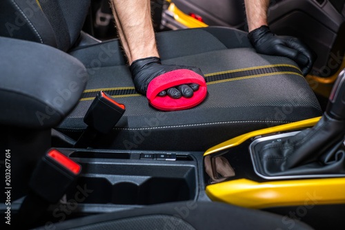 Cleaner hand scrubbing car seat with red sponge, deep cleaning and interior car wash concept
