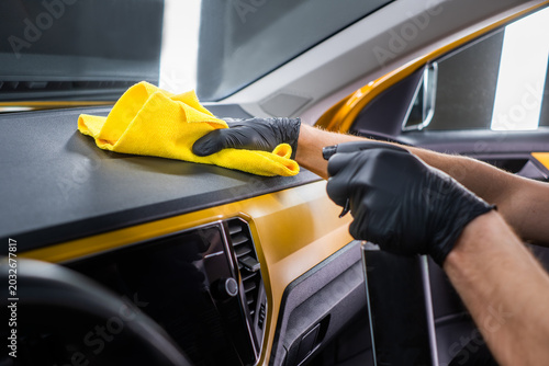 Cleaner hands cleaning car dashboard with yellow cloth and spray, interior car wash and vehicle cleaning concept

