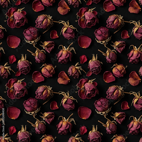 A seamless pattern of dried faded red roses and scattered petals on a dark black background texture in flat lay photography style.