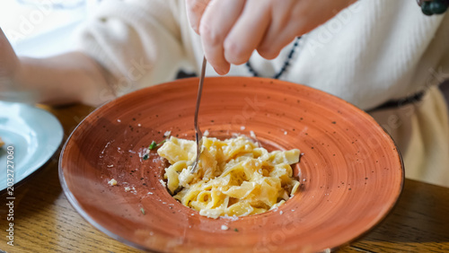 Fotografie Hands Twirling Creamy Pasta At Cafe, Terracotta Bowl Topped With Parmesan And Cr
