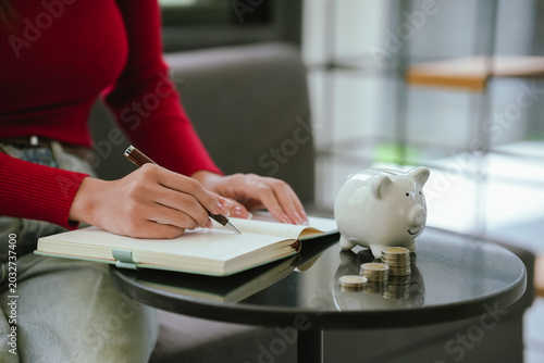 Woman using a smartphone beside a piggy bank and calculator, representing digital budgeting, saving money, and personal financial management.