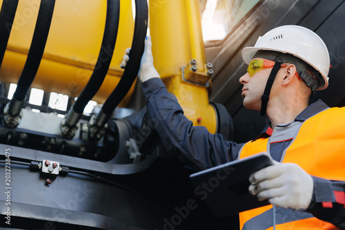 Εκτύπωση καμβά Engineer inspecting hydraulic system of machinery on construction site with tabl