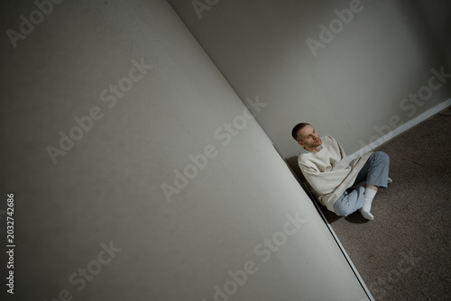 Photos High angle view of Caucasian young adult man sitting restrained in corner, conveying mental health crisis, isolation, psychiatric distress