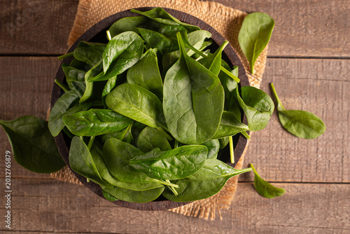 Green baby spinach leaves in wooden bowl on wooden background. Organic food concept. 