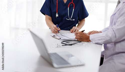 Foto Medical Team Collaborating in Clinic, Nurse in Blue Scrubs Pointing at Clipboard