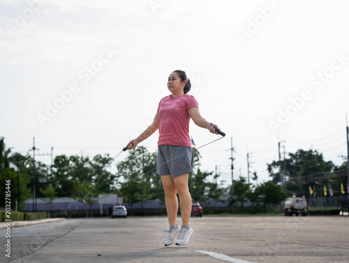 фотографія Young Asian woman in pink t-shirt skipping rope and jumping outdoors for fitness and weight loss