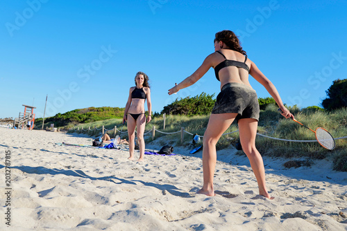 Friends having fun and playing badinton on the beach on a sunny day, action moves on the beach sand