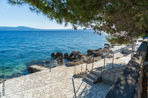 Fotografie Sunny seaside promenade with stairs and rocky Adriatic coastline in Novi Vinodolski, Croatia