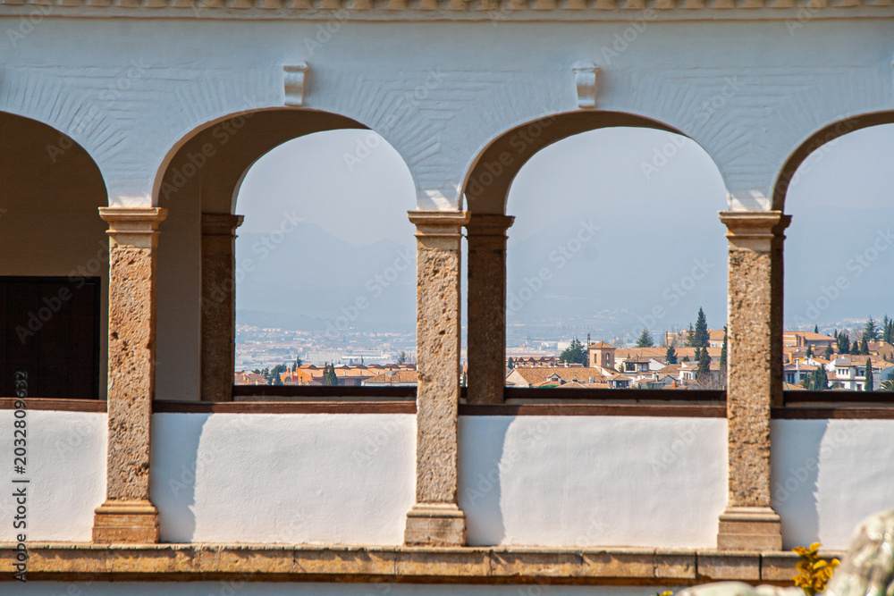 Naklejka premium Alhambra arches creating a historical viewpoint, framing the UNESCO World Heritage city of Granada and the traditional Albaicin neighborhood on a clear day in Spain