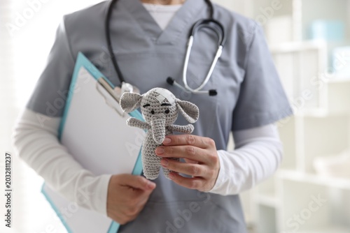 Quadro su tela Pediatrician holding toy elephant with adhesive bandages and clipboard in clinic