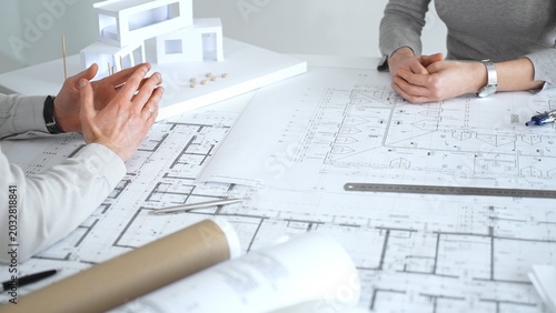 Fotografie Architects discussing architectural blueprints and a building model on a white d