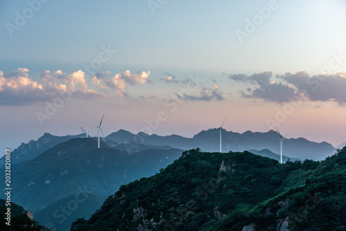 Wind turbines on mountain ridges in northern China at sunset, showcasing renewable energy and sustainable power generation.