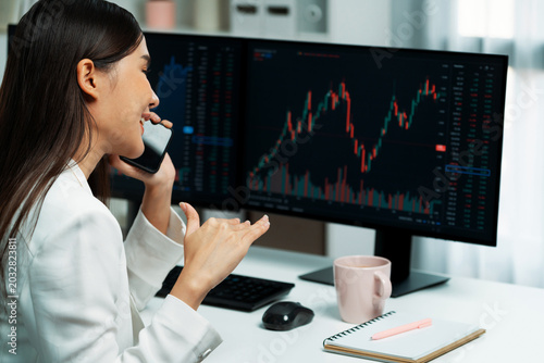 Φωτογραφία Young beautiful Asian businesswoman calling to broker on phone to analyze stable or higher profit value with profitable each exchange stock market graph on pc screens at modern office