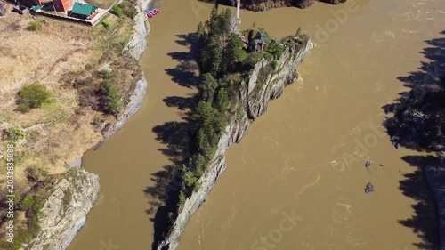 Aerial View Of Narrow River Island Showing Rocky Triangular Islet With Dense Trees And Muddy River, Riverside Cottages On Banks, Ecologist Drone Scout Documenting Erosion, Calm Midday Light