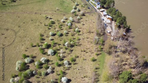 Aerial View Of Riverside Valley Cottages And Winding Road Along Muddy River, Pastoral Fields And Orchard Patches, Rural Homestead Lifestyle And Agrotourism Potential Captured By Drone, Peaceful Spring