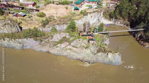 Aerial View Of Riverside Peninsula And Bridge With Adjacent Village Rooftops, Rocky Shoreline And Boat Moored Near Cliff, Bridge Inspector Drone Capturing Connectivity And Rural Access Points, Bright