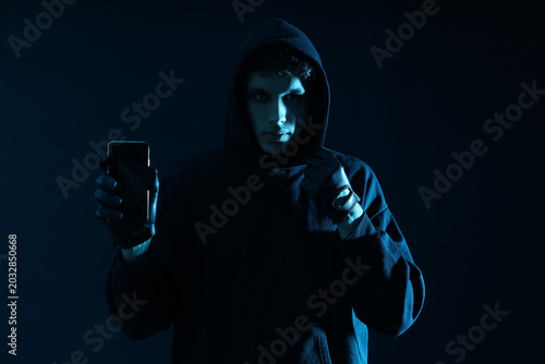 Slika na platnu Male fraudster with mobile phone on dark background