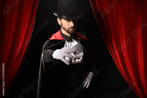 Foto Male magician with playing card near red curtains on dark background