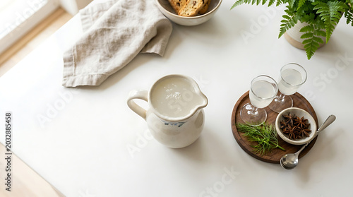 Small ceramic pitcher with handle and spout filled with liquid, placed on a white table with accompaniments