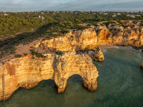 Drone view of Praia da Marinha beach in Algarve, Portugal, with golden cliffs, sea arches, turquoise Atlantic water, and coastal rock formations.