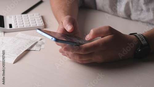 Hands Holding Phone Over Receipts, Calculator Nearby, Freelancer Reviewing Expenses For Side Hustle, Soft Warm Lighting, Neutral Desk Background, Closeup Focused Workflow