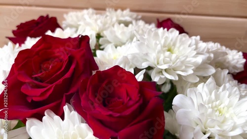 Red roses and white chrysanthemums arranged in a vibrant floral bouquet, showcasing the intricate details of petals and leaves against a natural wooden background