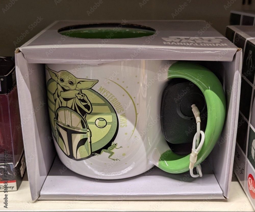 Naklejka premium Taza oficial de la serie The Mandalorian de Star Wars, con el dibujo de Grogu y del casco del Mandalorian, en estante de juguetería Toy Planet en Madrid, España, 7 de abril de 2026