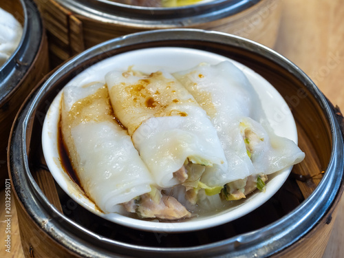 Photography Steamed rice noodle rolls dim sum served in bamboo basket, featuring halal Chinese cuisine, soft texture, savory filling, and traditional Asian food concept in restaurant dining setting