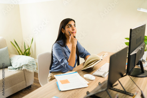 Foto Young woman with long dark hair thinking, looking up while holding a pen, sittin