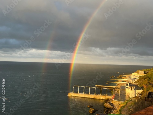 Double rainbow over the sea with sunlit seafront after rain