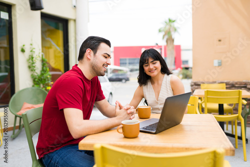 Young adults working together at outdoor cafe, using laptop for remote work and digital collaboration