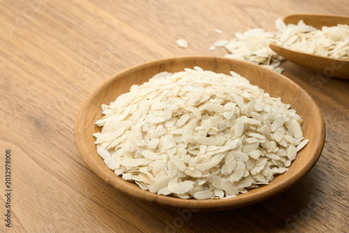 Raw white flattened rice flakes or Poha served in a wooden bowl on a timber table. This organic cereal is a popular Indian breakfast ingredient, perfect for healthy food and cooking background