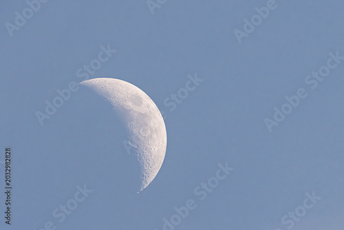 Visual representation of crescent moon with prominent craters and twilight background