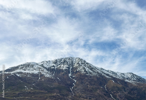 Majestic snow-capped Altai Mountains under a bright blue sky with clouds in Xinjiang, China.