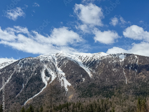 Majestic snow-capped Altai Mountains under a bright blue sky with clouds in Xinjiang, China.