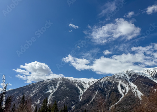 Majestic snow-capped Altai Mountains under a bright blue sky with clouds in Xinjiang, China.
