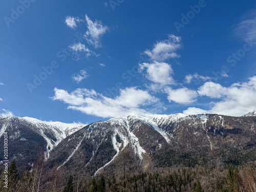 Majestic snow-capped Altai Mountains under a bright blue sky with clouds in Xinjiang, China.