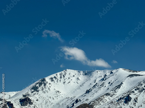 Majestic snow-capped Altai Mountains under a bright blue sky with clouds in Xinjiang, China.