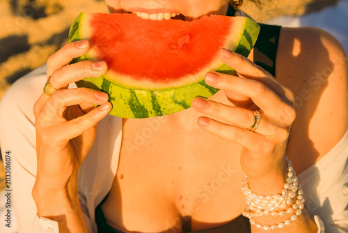 Schilderij op canvas Eating watermelon on beach during sunset with hands holding  slice and wearing jewelry on  wrist