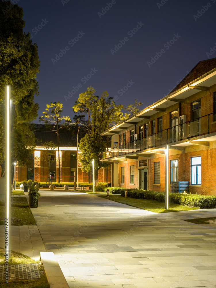 Fototapeta premium Empty paved pedestrian street lined with illuminated brick buildings and modern streetlights at night