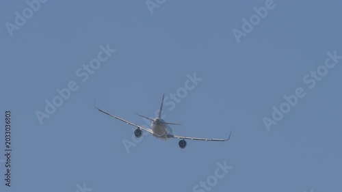 A commercial passenger jet airplane climbing high into a clear solid blue sky. Rear perspective view showing the tail, engine exhausts, and winglets on the wingtips during a smooth flight departure.