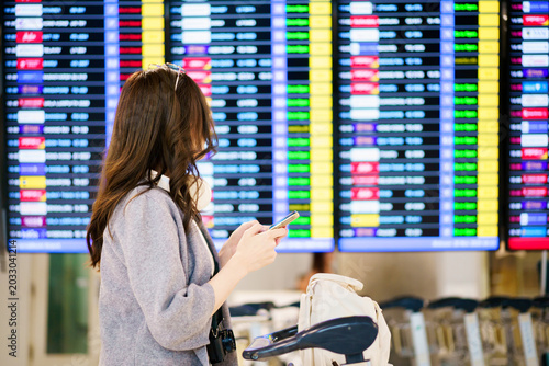 Foto Asian woman holding passport and boarding pass while checking flight schedule