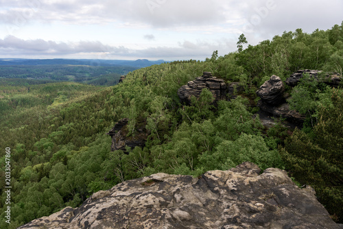 Dramatic morning view from Grosser Zschirnstein, Saxon Switzerland, Germany, with distant horizon, layered clouds, deep forest below and sandstone rocks in foreground.