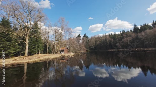 fpv drone dlying over pond and around wood cabin in Vosges region on a sunny spring day