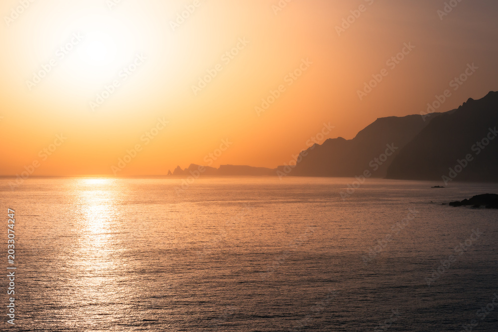 Fototapeta premium Bright golden sunrise over calm ocean horizon with distant coastal cliffs.