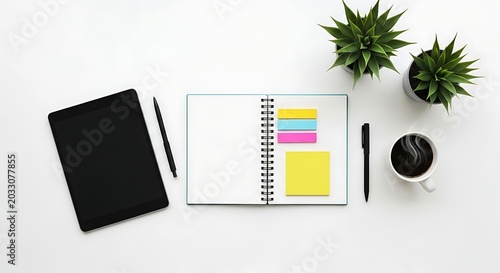 Top view of a workspace with a tablet, notebook, pens, coffee, and plants