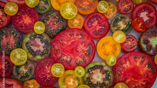 Fresh tomatoes are displayed on a table in various shapes and colors during a summer gathering for local produce