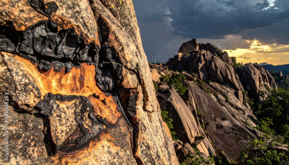 Obraz premium Dramatic Mountainous Landscape with Charred Granite Rocks Under Stormy Sunset Sky