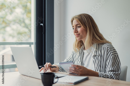 Cuadro en lienzo Young blonde woman teleworking from a modern home office, typing on a laptop and